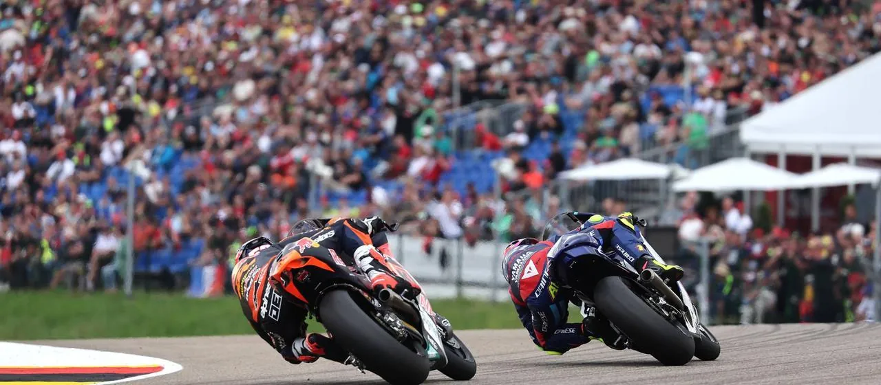Zwei Motorräder fahren vor einer vollbesetzten Tribüne über den Sachsenring